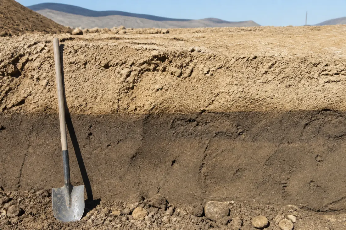 A cut bank on a building pad showing a sharp line between placed fill above and undisturbed soil below
