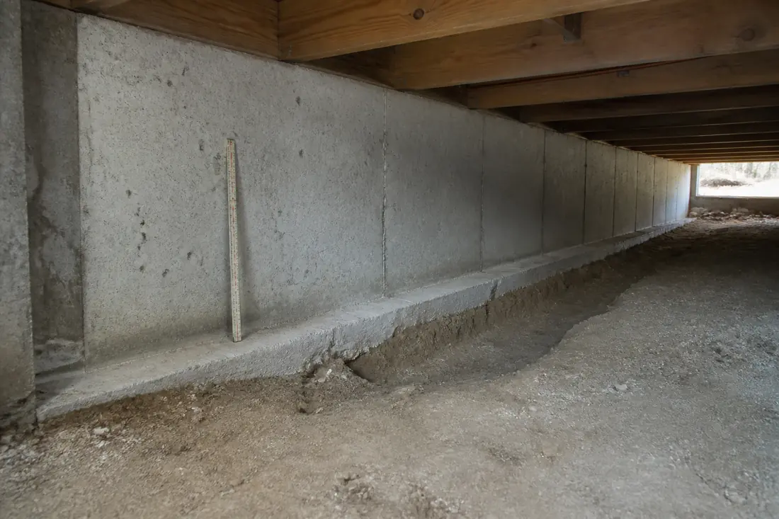 The interior of an unfinished crawl space showing the top of a strip footing against the bare earth floor