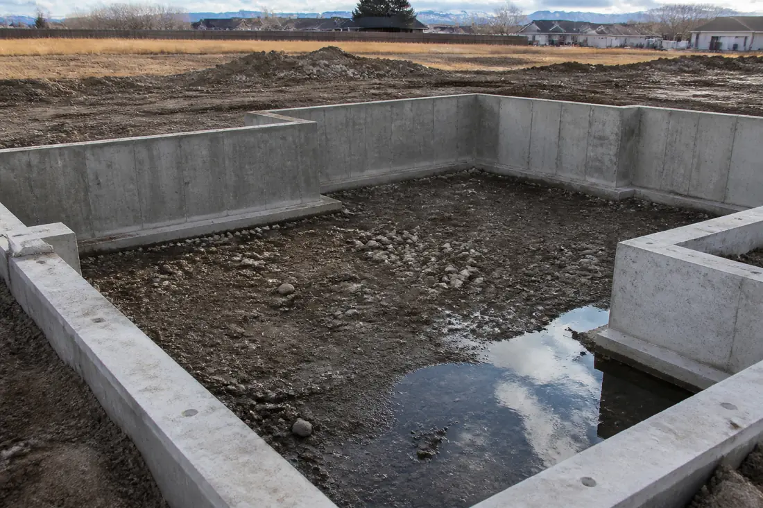 An unfinished crawl space foundation with poured stem walls and a shallow pool of standing water in one corner