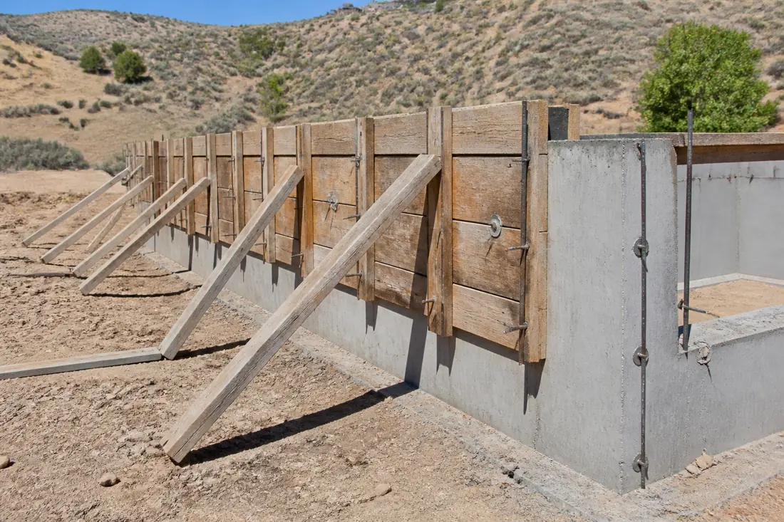 Timber formwork braced against a freshly poured concrete foundation wall