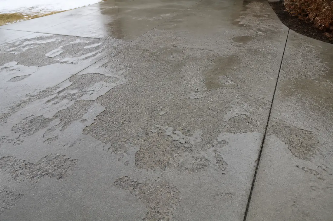 Concrete driveway surface with the top layer flaked away exposing sand and aggregate